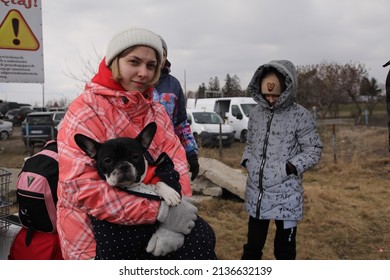 Medyka, Poland - March 10, 2022: A young Ukrainian woman fleeing the Russian invasion waits with her dog and family to board a bus just across the border to take them to their next stop.