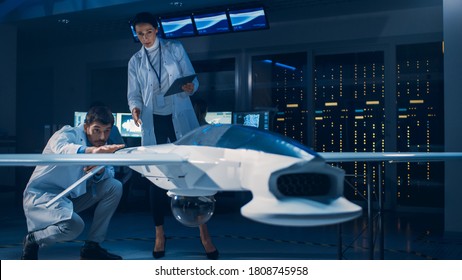 Meeting of Aerospace Engineers Working On Unmanned Aerial Vehicle / Drone Prototype. Aviation Scientists in White Coats Talking. Commercial Aerial Surveillance Aircraft in Industrial Laboratory