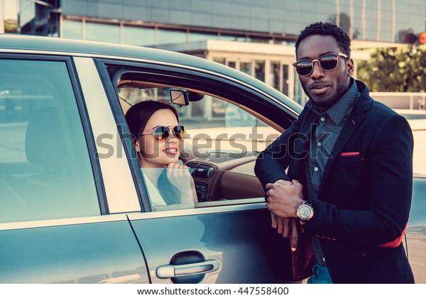 Meeting of black casual man and caucasiand business\
woman near a car.