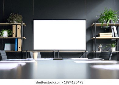 Meeting conference room with blank empty mockup tv screen monitor for advertising standing in modern contemporary office on black wall background. No people. Business technologies concept.