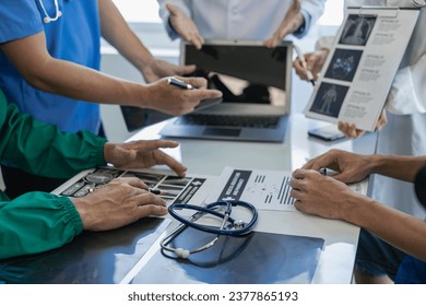 Meeting with doctor in white lab coat and surgical scrubs sitting at table discussing patient records. Team of doctors working on digital tablet, doctors tablet technology using computer - Powered by Shutterstock