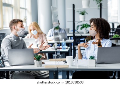 Meeting during work. Guy and african american woman in protective masks talking about marketing through glass board at workplace with laptops and antiseptic in interior of office during COVID-19 - Shutterstock ID 1818838538