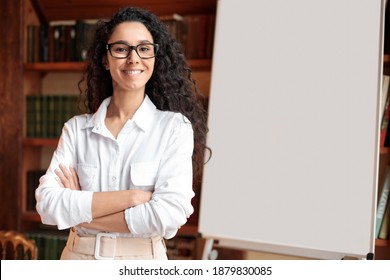 Meeting And Education. Portrait Of Smiling Young Lady In Eyewear Standing With Folded Arms And Posing At Camera Near Blank Empty White Board In The Background. Happy Casual Woman In Shirt