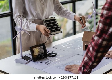 Meeting of female engineers and developers of renewable energy systems with solar panels and tabletop model houses. to design the use of renewable energy with wind turbines and solar - Powered by Shutterstock