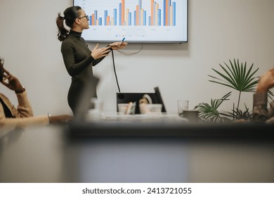 In a meeting indoors, a young woman captivates the room, discussing key points with coworkers, fostering a dynamic presentation.