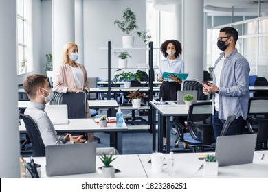 Meeting With Manager And Protecting Health After Returning To Office After Quarantine. Boss In Protective Mask With Tablet Speaks To Multiracial Of Workers In Office Interior With Devices, Empty Space