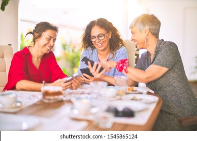 Meeting Of Middle Age Women Having Lunch And Drinking Coffee. Mature Friends Smiling Happy Using Smartphone At Home On A Sunny Day