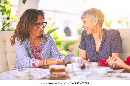 Meeting Of Middle Age Women Having Lunch And Drinking Coffee. Mature Friends Smiling Happy Using Smartphone At Home On A Sunny Day