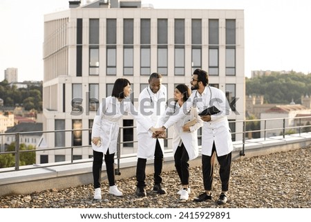 Meeting of multinational doctors in modern clinic during break. Group of successful medics celebrating success by touching hands as team sign together outdoors near modern hospital.