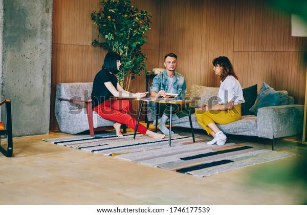 Meeting of professional designers in modern
apartment interior, casual dressed male and female colleagues
collaborating on common project having brainstorming course for
productive developing