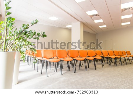 Meeting room interior.  Front view of rows of orange chairs standing in an auditorium. Seats in an empty conference room. Huge Hall interior with carpet and lights as conference hall in luxury hotel.