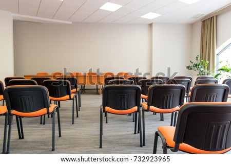 Meeting room interior.  Front view of rows of orange chairs standing in an auditorium. Seats in an empty conference room. Huge Hall interior with carpet and lights as conference hall in luxury hotel. 