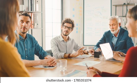 In The Meeting Room Young And Beautiful Female Junior Associate Makes A Speech / Report To A Board Of Directors Member Who Are Sitting At The Conference Table. Modern Startup In The Stylish Office