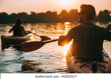 La puesta del sol en kayaks. Vista trasera de una pareja joven kayak en el lago junto con puesta de sol en el fondo