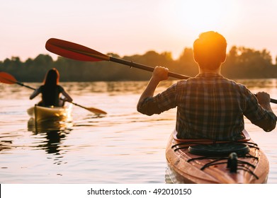 Meeting sunset on kayaks. Rear view of beautiful young couple kayaking on lake together with sunset in the background - Powered by Shutterstock