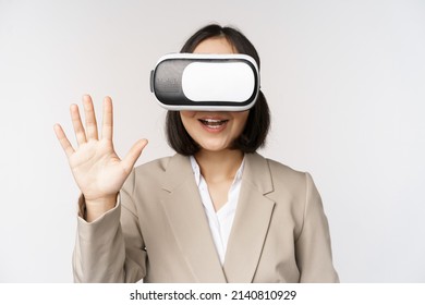 Meeting in vr chat. Asian businesswoman in virtual reality glasses, waving hand and saying hello, greeting someone, standing over white background