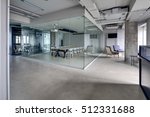 Meeting zone in the office in a loft style with white brick walls and concrete columns. Zone has a large wooden table with gray chairs and glass partitions. Above the table there is a projector. 