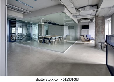 Meeting Zone In The Office In A Loft Style With White Brick Walls And Concrete Columns. Zone Has A Large Wooden Table With Gray Chairs And Glass Partitions. Above The Table There Is A Projector. 