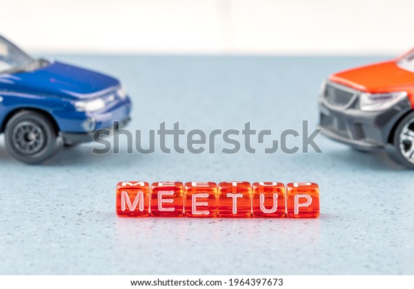 Meetup written on red cubes in\
the background out of focus two cars. like-minded people\
meet