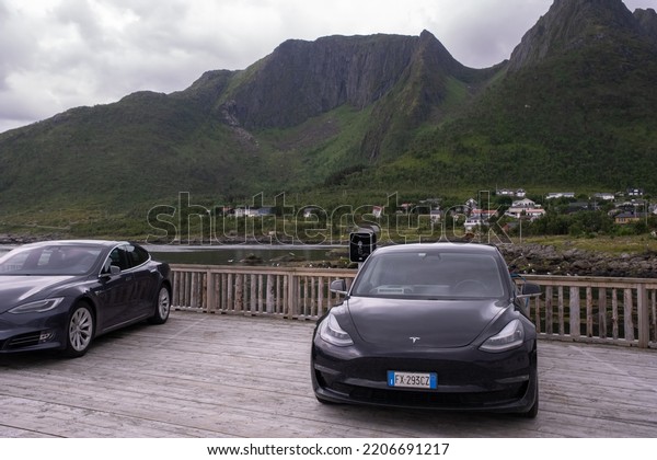 Mefjordvaer,\
Norway - July 21, 2022: A static shot of a solid black Tesla Model\
3 dual motor charging at the Mefjordvaer port AC charging station\
in a cloudy summer day. Selective\
focus.