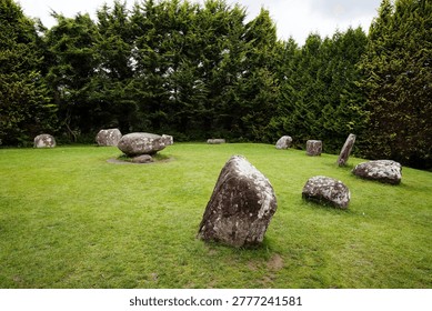 Megalithic stone circle with dolmen structure on lush grass, bordered by tall green trees
