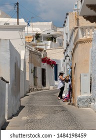 Megalochori, Greece - July 17 2019:   A Shop Keeper Arranges Her Display Items Outside A Small Boutique In The Back Streets Of Megalochori