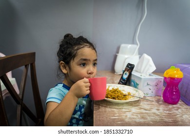 Melaka , Malaysia - Circa October 2020:A Malay Girl Drinking A Milk From A Cup In A Kitchen; With Her Smartphone Bin Background 