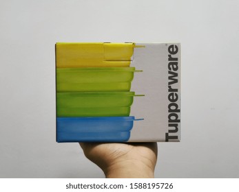 Melaka, Malaysia - December 14, 2019: A Hand Holding A Tupperware Box Against White Wall Background.