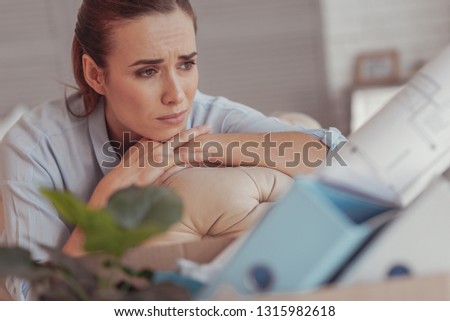 Melancholic. Close up of dispirited young woman resting her chin on hands and averting her sad glance while sitting on sofa