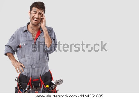 Melancholic depressed overworked young manual worker has headache, poses with downhearted expression, wears casual outfit, stands against white background with copy space for your advertisement