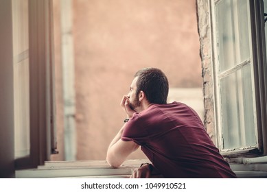 Melancholic and lethargic man looking outside through a big window, contemplating his emotional or mental problems in life