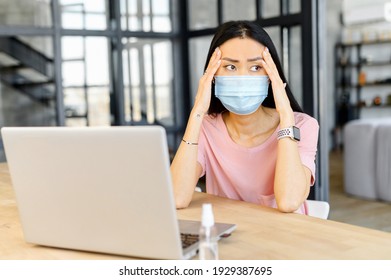 Melancholy Asian Woman With A Face Covered Feels A Headache, A Female Office Employee Wearing Protective Mask Holding Head, Massaging Temples, Has Migraine