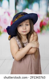 Melancholy Little Girl In Too Big Hat Cringed With Crossed Arms