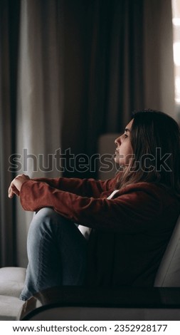 Melancholy young woman sitting on coach with tranquil expression