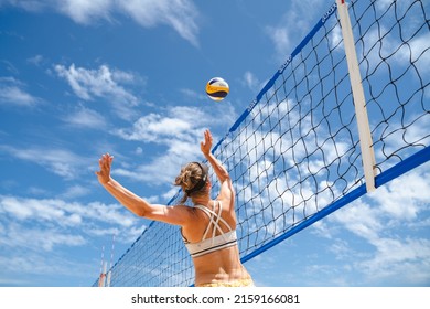 MELBOURN, AUSTRALIA - Dec 06, 2021: A low angle shot of a volleyball player jumping against the net to hit the ball in bright sunlight against the blue cloudy sky in Melbourne, Australia