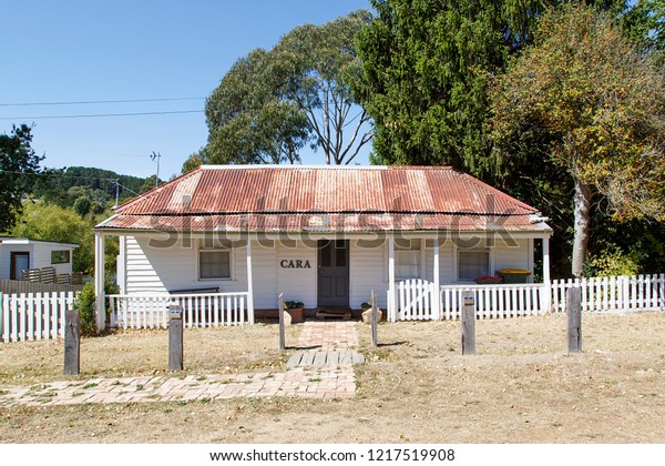 Melbourne,\
Australia: March 23, 2018: A typical detached double fronted\
bungalow home with a red corrugated roof, white picket fence and\
verandah in Daylesford - Australia.\
