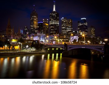 Melbourne Skyline with a reflection in the water of a couple standing on the bridge.