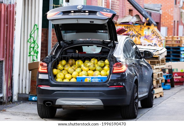 Melbourne,\
Victoria, Australia - 06.10.2021: A car with a boot load of  large\
citrus fruit is parked at the back of a fruit and vegetable market\
amongst wooden pallets and other\
junk.