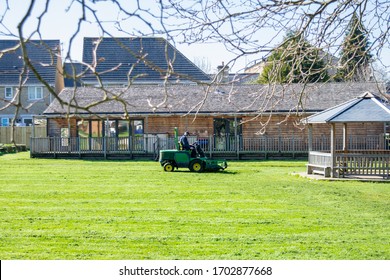 Melksham Wiltshire UK March 25 2020 A Man On A Ride On  Lawnmover Cutting The Grass Of A Primary School Field  While The Children Are Not At School