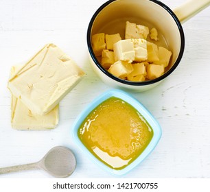 Melted Butter In Light Blue Dish, Two Bars Of Milk Butter And A Pan With Pieces Of Butter For Melting On White Wooden Table, Ayurvedic Food For Everyday, Flat Lay, Top View, Closeup