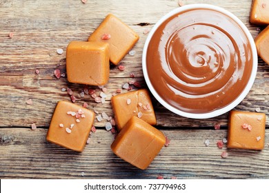 Melted caramel with pieces of caramel candy with salt on a wooden table.