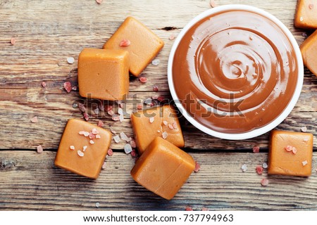 Melted caramel with pieces of caramel candy with salt on a wooden table.