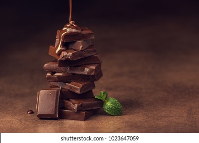 geschmolzene Schokolade, die zu einem Stück Schokoladenriegel mit grünem Minzblatt auf einem Tisch gießt