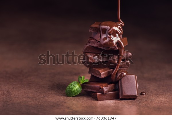 melted chocolate pouring into a piece of\
chocolate bars with green mint leaf on a\
table