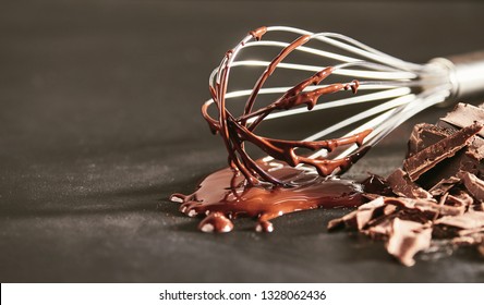 Melted dairy chocolate dripping off an old whisk onto a rustic kitchen table with chopped bar of cooking chocolate alongside