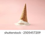 Melted ice cream in wafer cone on light pink background