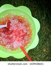 A Melting Cherry Snowcone Sitting In The Grass.