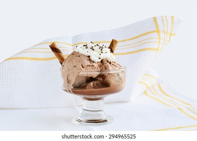 Melting chocolate ice-cream in glass bowl over white cloth.