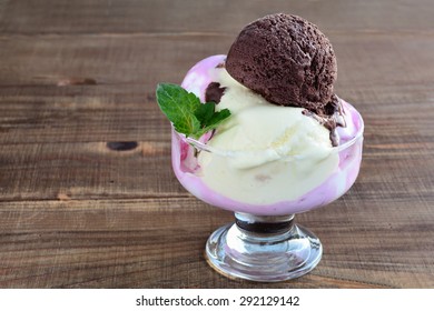 Melting chocolate, strawberry and yogurt ice-cream in glass bowl on wooden background.