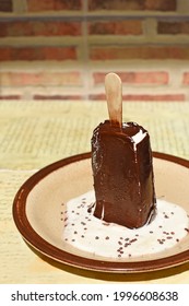 A Melting Chocolate-covered Popsicle On A Stick Stands Upright On A Saucer In A Puddle Of Milky White Softness.